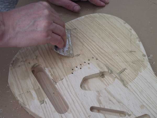 Scraping excess grain filler from the front of the guitar body